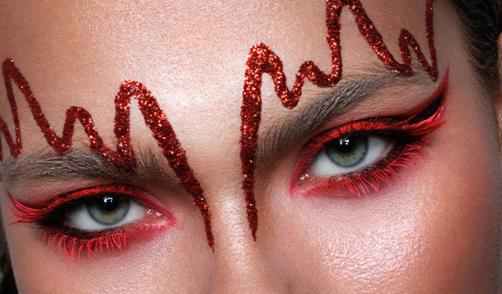 Nahaufnahme von Augen mit rotem Glitzer-Make-up und kunstvollem roten Muster über den Augenbrauen.