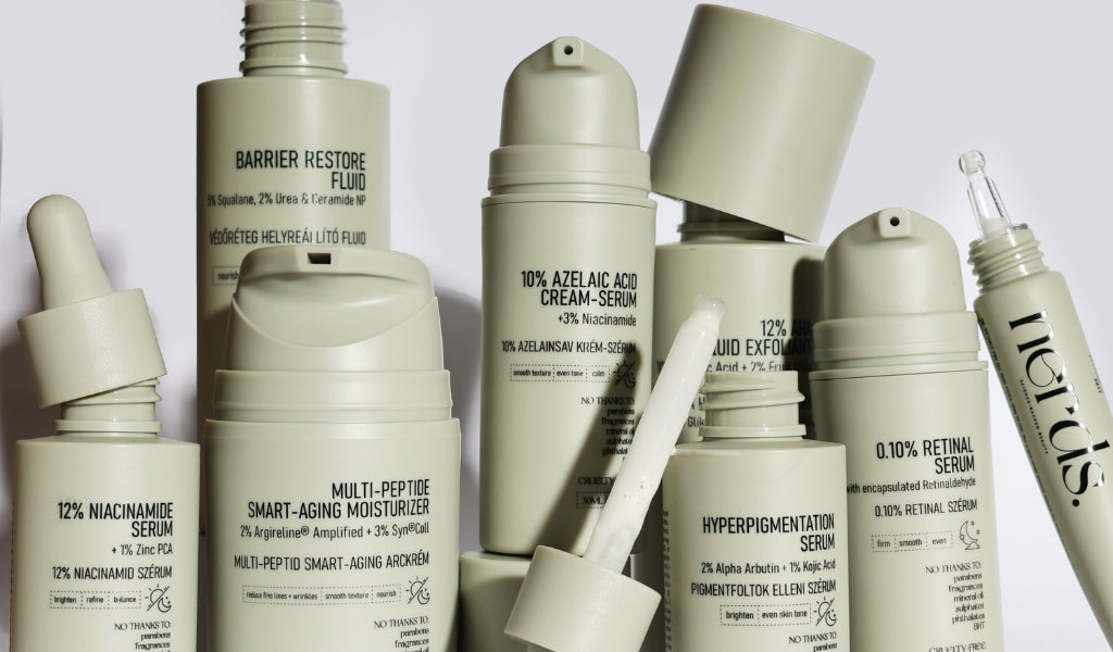Mehrere minimalistische Hautpflegeprodukte in hellen Flaschen, darunter Seren, Cremes und Exfoliant, dicht nebeneinander.