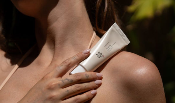 Hand hält Beauty of Joseon Relief Sun Sonnencreme vor sonnengebräunter Schulter im warmen Tageslicht.