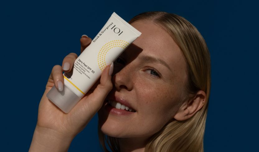 Blonde Frau hält die Geek & Gorgeous Zero Feel Sonnencreme mit LSF 50 vor ihr Gesicht.