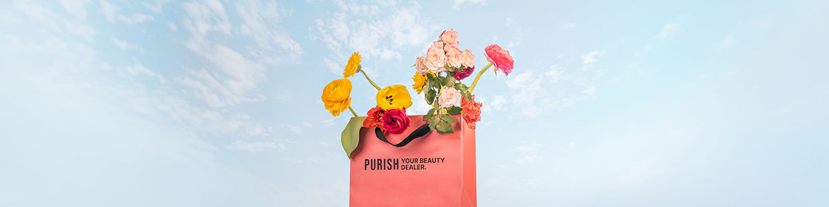Eine rosafarbene Einkaufstasche mit der Aufschrift "PURISH" steht vor einem blauen Himmel mit leichten Wolken. Aus der Tasche ragen bunte Blumen.