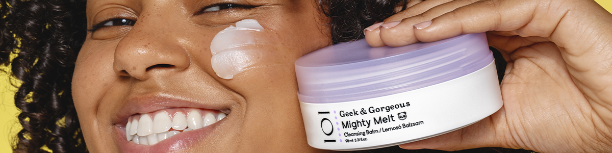 Lächelnde Frau trägt Gesichtsbalsam auf und hält einen Tiegel von Geek & Gorgeous Mighty Melt in der Hand.