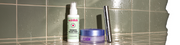 Skinlick Redness Relief Mist, Xlash Longevity Multi-Zone Gels und eine Xlash-Tube, die auf einer gefliesten Oberfläche mit Wassertropfen steht.