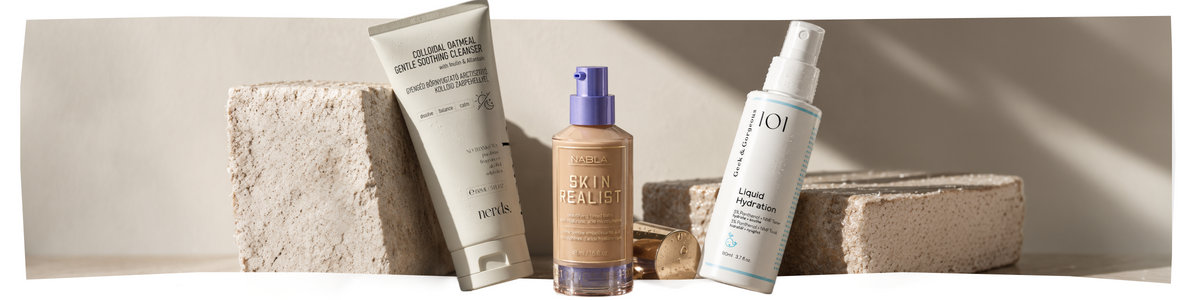 Drei Hautpflegeprodukte – Creme, Serum und Spray – sind aufrecht auf beigen, strukturierten Steinblöcken ausgestellt, bei neutraler Beleuchtung und mit einem sanften Schatten im Hintergrund.