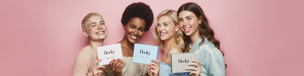 Vier lächelnde Frauen halten Fleeky-Produktboxen vor einem rosa Hintergrund.