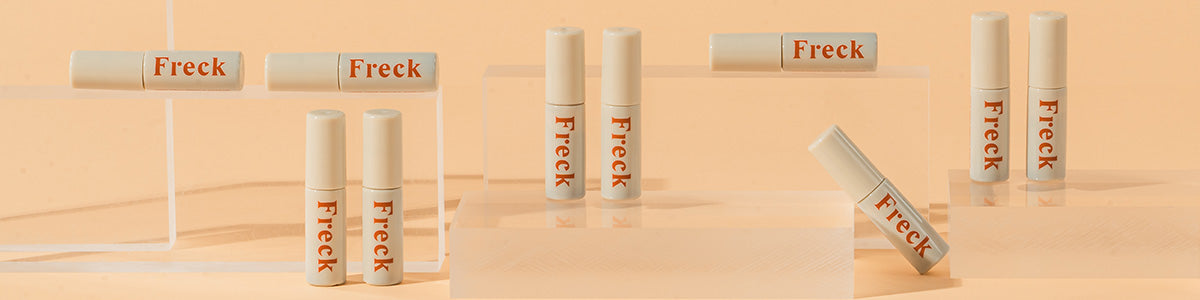 Mehrere beige Tuben mit der Aufschrift ‚Freck‘ auf transparenten Podesten vor pfirsichfarbenem Hintergrund.