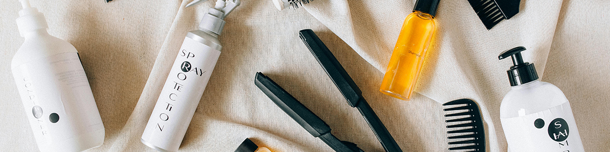 Haarstyling-Werkzeuge, Kämme, Sprühflaschen und Haarprodukte, die auf einem hellen Stoffhintergrund angeordnet sind.