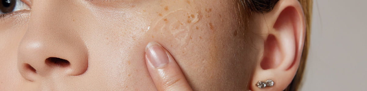 Nahaufnahme einer Person, die mit ihrem Zeigefinger ein Serum auf ihrer Wange verteilt.