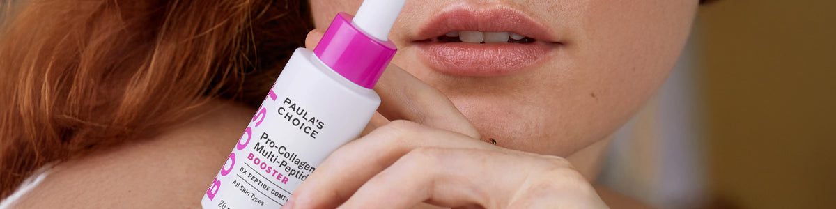 Eine Frau hält eine Flasche Paula’s Choice P.C. Multi-Peptide Booster schräg vor ihrem Gesicht (Mundbereich). .
