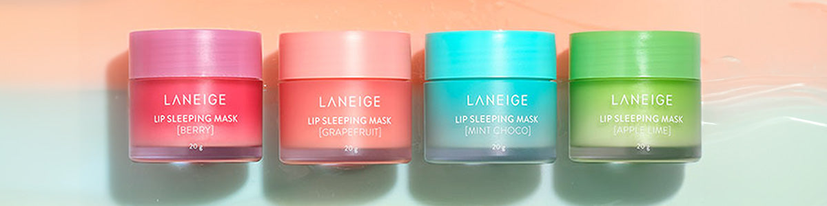 Vier farbige Tiegel der LANEIGE Lip Sleeping Mask in den Sorten Berry, Grapefruit, Mint Choco und Apple Lime auf pastellfarbenem Hintergrund.