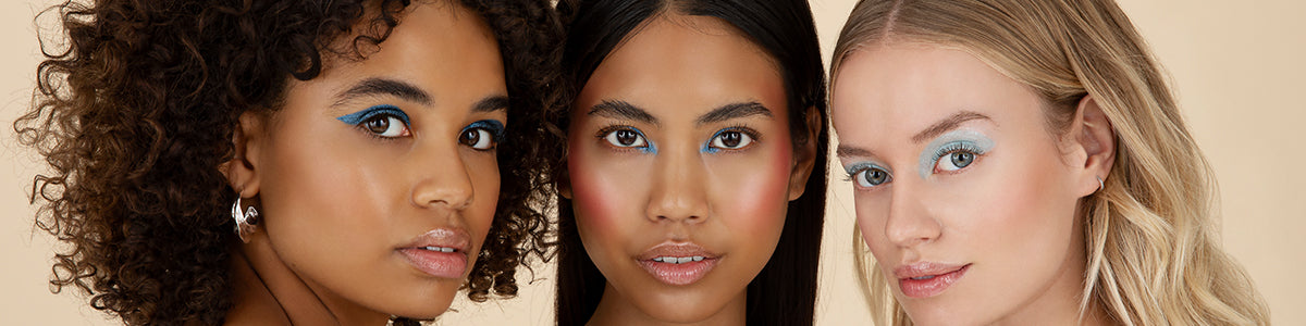 Drei Frauen mit unterschiedlichem Hautton tragen blauen Lidschatten und natürliches Make-up und posieren eng beieinander.