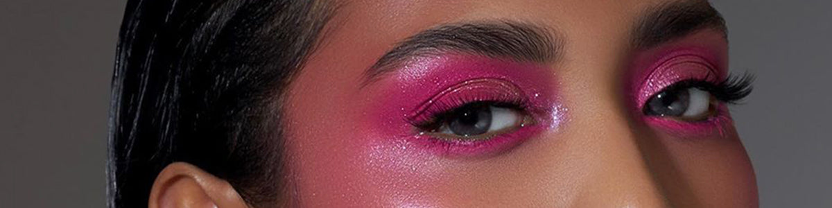 Nahaufnahme des Gesichts einer Person mit schimmerndem rosa Lidschatten und kräftigen, definierten Augenbrauen.