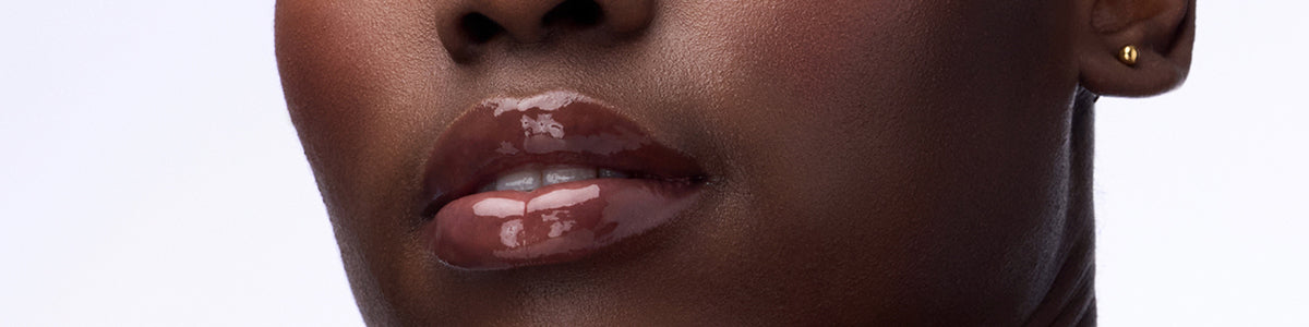 Nahaufnahme der glänzenden Lippen, eines Teils der Nase und der Wange einer Person, mit sichtbarem goldenen Ohrstecker.