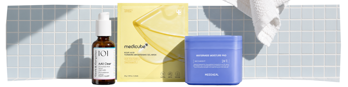 Drei Hautpflegeprodukte – ein Serum, eine Schachtel mit Gesichtsmasken und ein Tiegel mit blauer Creme – sind vor blauen Fliesen angeordnet, im Hintergrund ist ein weißes Handtuch zu sehen.