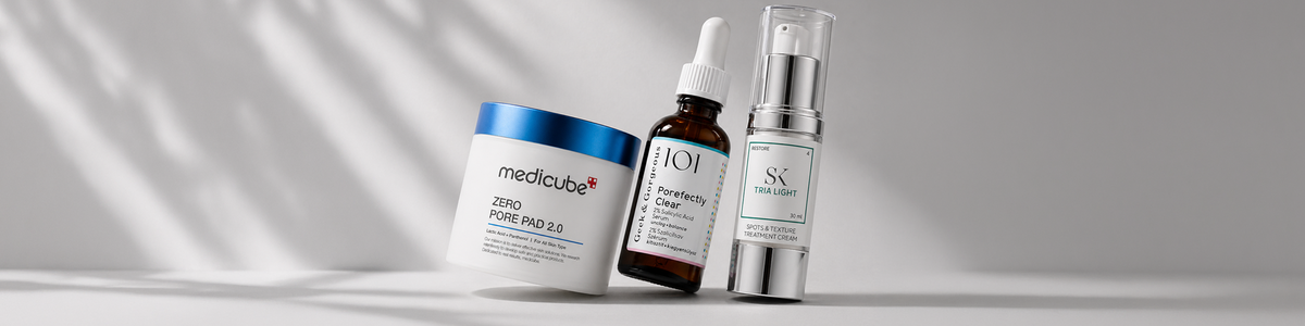 Drei Hautpflegeprodukte – ein „Medikube“-Tiegel, eine braune Tropfflasche und eine silberne Pumpflasche – sind auf einer weißen Fläche angeordnet, im Hintergrund sind sanfte Schatten zu sehen.