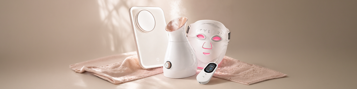Verschiedene Schönheitsgeräte und Hautpflegetools, darunter eine LED-Maske, auf rosa Hintergrund präsentiert.