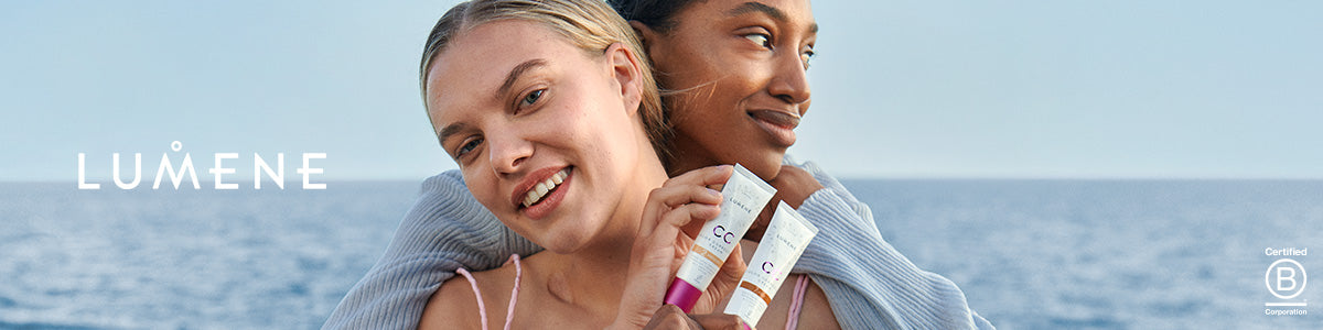 Zwei lächelnde Personen umarmen sich am Meer und halten CC-Creams der Marke Lumene in den Händen.