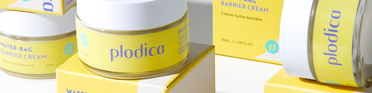 Mehrere Tiegel der Water-Bag Barrier Cream von Plodica in gelber Verpackung, dekorativ auf Kartons arrangiert.