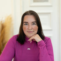 Porträt von Melanie mit dunkelbraunen Haaren und violettem Rollkragenoberteil vor hellem Hintergrund.
