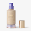 Eine Flasche Skin Realist Tinted Balm in der Farbe 1 Fair mit einem violetten Pumpspender und einem goldenen Deckel daneben.