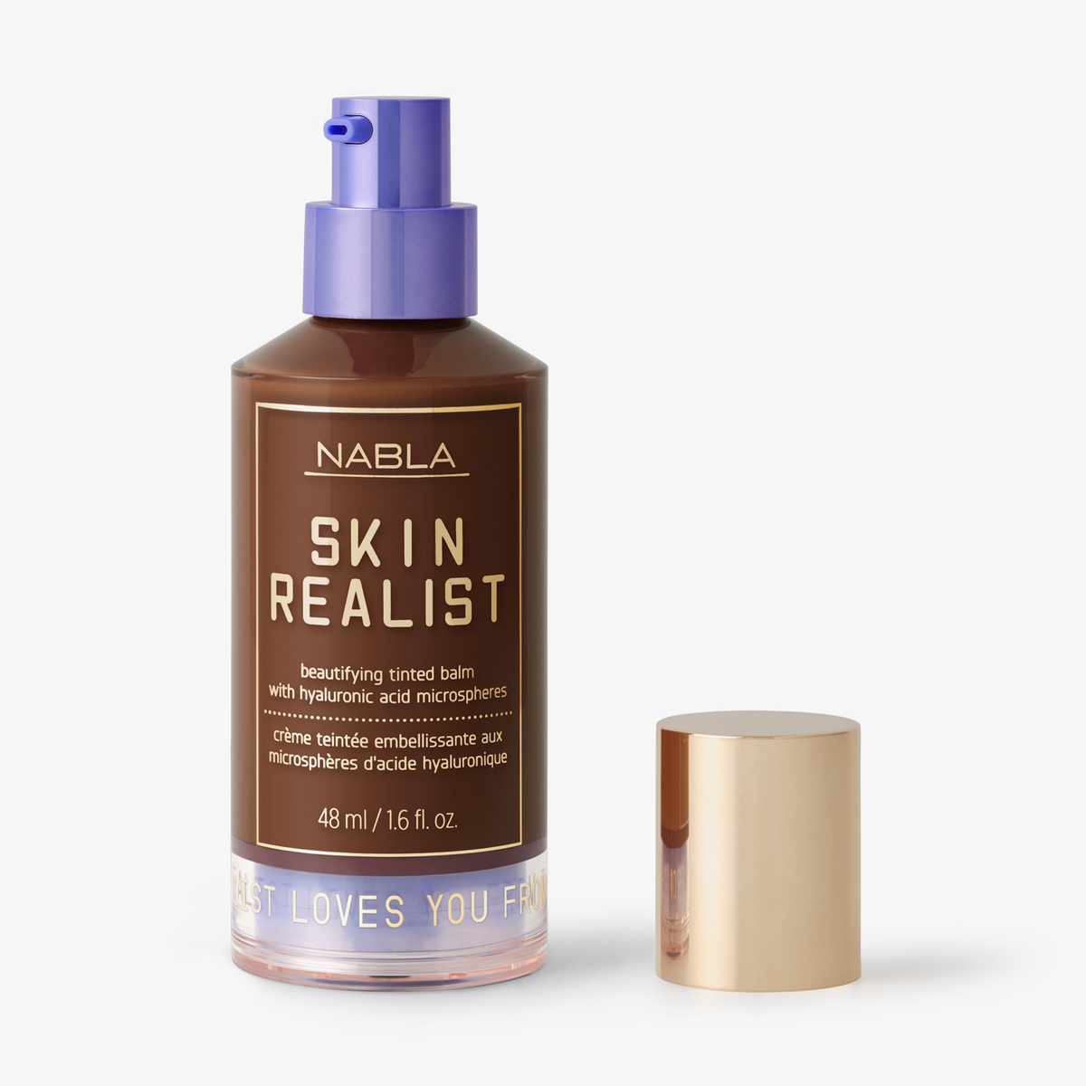 Eine Flasche Skin Realist Tinted Balm in der Farbe Deep mit einem violetten Pumpspender und einem goldenen Deckel daneben.