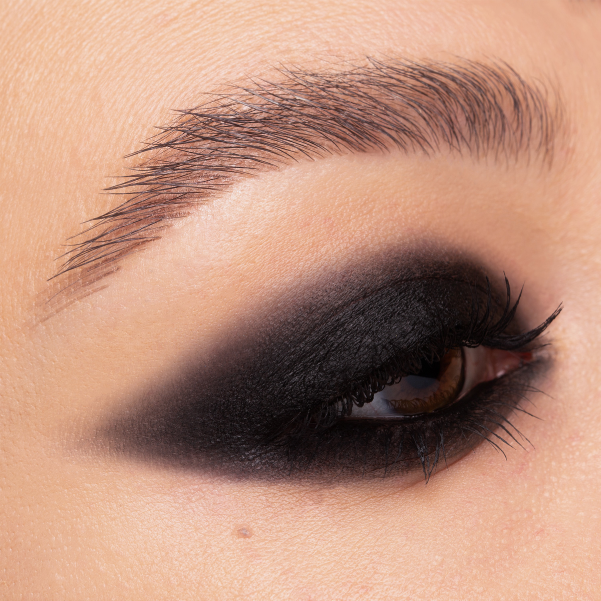 Nahaufnahme eines Auges mit intensivem, mattem schwarzen Smokey-Eye-Make-up und definierten Wimpern auf heller Haut.