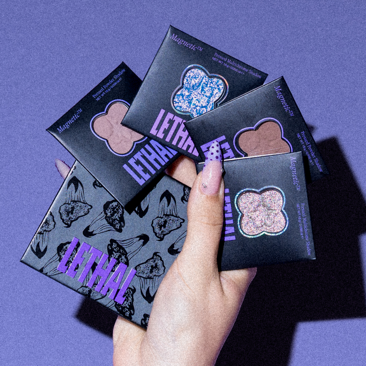 Eine Hand mit lila lackierten Fingernägeln hält die „PURISH x Lethal Palette Birthday Edition“ von Lethal Cosmetics vor einem lila Hintergrund.