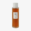 Eine transparente Flasche Ginseng Essence Water mit weißem Deckel und bernsteinfarbener Flüssigkeit vor weißem Hintergrund