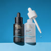 Zwei Flaschen Bondi Sands Self Tan Drops, eine dunkle und eine helle, stehen vor einem blauen Hintergrund