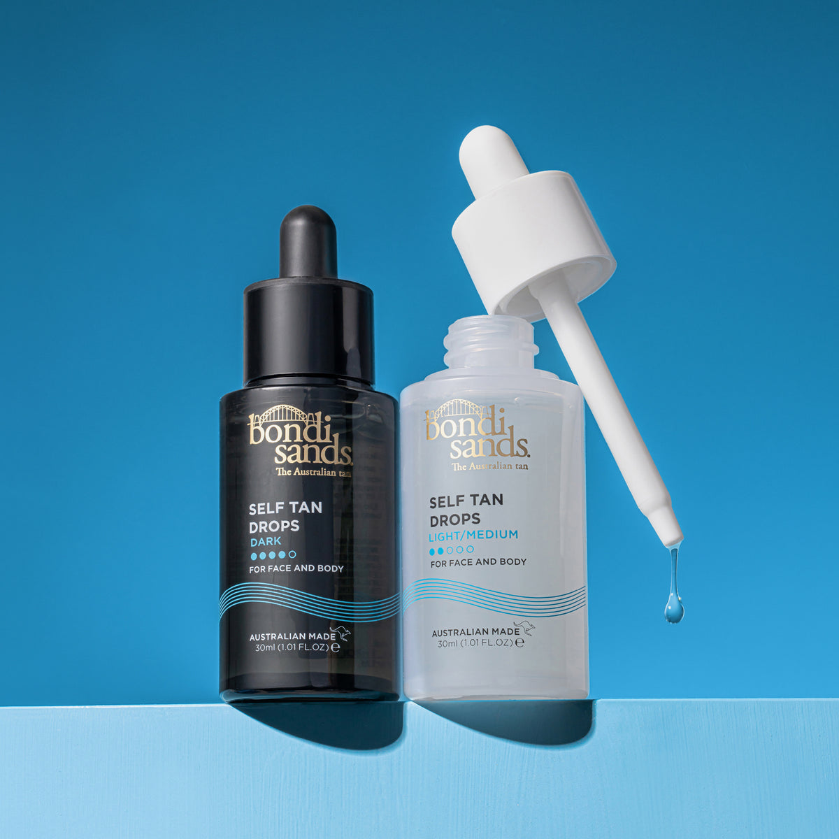 Zwei Flaschen Bondi Sands Self Tan Drops, eine dunkle und eine helle, stehen vor einem blauen Hintergrund