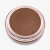 Ein runder offener Behälter mit Cronzer Cream Bronzer Acron mit braunem Inhalt auf weißem Hintergrund.