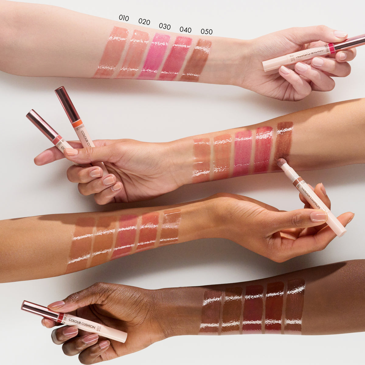 Swatches von fünf Catrice Colour Cushion Juicy Lip Oils (010–050) auf vier unterschiedlich getönten Armen, jede Farbe wird mit dem jeweiligen Lip Oil aufgetragen.