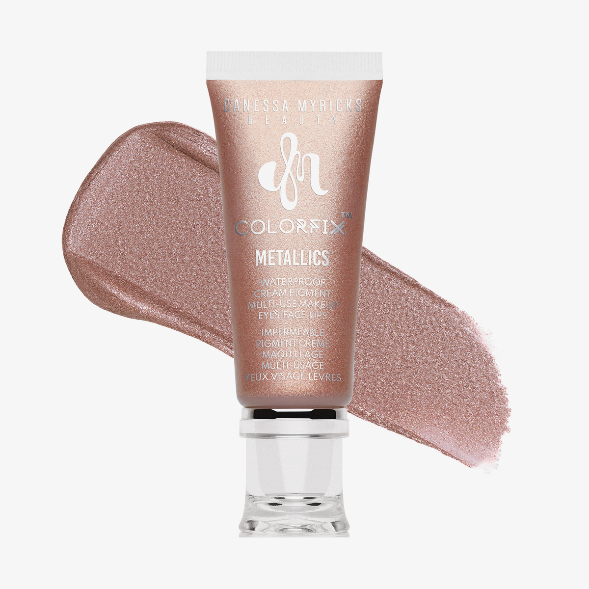 Eine Tube Danessa Myricks Beauty Colorfix Metallics in Ballerina mit einer Probe des roségoldenen Cremepigments dahinter.
