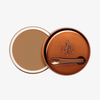 Runder geöffneter Behälter Yummy Skin Blurring Balm Shade 4.5 mit bronzefarbenem Deckel und kleinem Applikator.