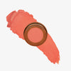 Yummy Skin Blurring Balm Powder Flushed Bellini in rundem bronzenem Behälter auf pfirsichfarbenem Farbmuster abgebildet.