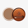 Runder geöffneter Behälter Yummy Skin Blurring Balm Shade 5.5 mit bronzefarbenem Deckel und kleinem Applikator.