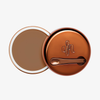 Runder geöffneter Behälter Yummy Skin Blurring Balm Shade 6.5 mit bronzefarbenem Deckel und kleinem Applikator.