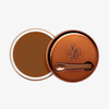 Runder geöffneter Behälter Yummy Skin Blurring Balm Shade 8.5 mit bronzefarbenem Deckel und kleinem Applikator.