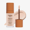Eine transparente Flasche Yummy Skin Lift & Flex Concealer 1 neben einem bronzenen Applikator vor hellbeigem Farbmuster.