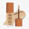 Eine transparente Flasche Yummy Skin Lift & Flex Concealer 4 neben einem bronzenen Applikator vor beigem Farbmuster.