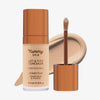 Eine transparente Flasche Yummy Skin Lift & Flex Concealer 6 neben einem bronzenen Applikator vor beigem Farbmuster.