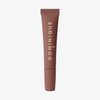 Eine braune Tube Juicy Lip Balm von Dominique Cosmetics mit senkrecht aufgedrucktem Markennamen in Weiß.