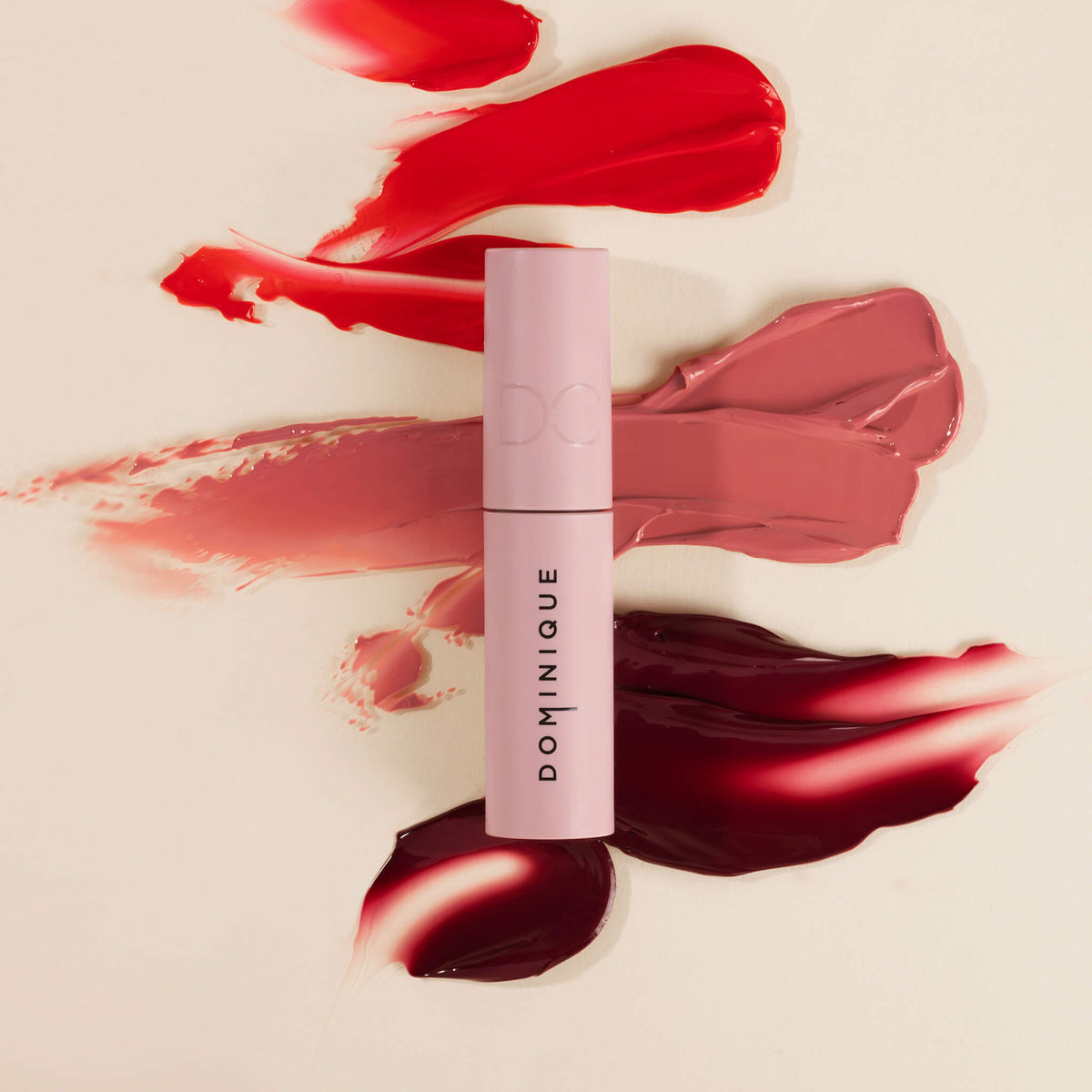 Eine Tube Pillow Soft Hydrating Lip & Cheek Stain in Pink auf cremefarbenem Hintergrund, akzentuiert mit roten, rosa und burgunderfarbenen Strichen.
