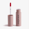Öffnen Sie die rosafarbene Tube Pillow Soft Hydrating Lip & Cheek Stain mit aufrecht stehendem Lippenstiftstab und dem Text DOMINIQUE an der Seite.