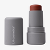 Eine graue Tube LH Cosmetics Artistick Blush in Abstract mit abgenommener Kappe, die den rötlich-braunen Rouge-Stift enthüllt.