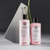 Zwei rosa Flaschen maria nila Luminous Colour Shampoo und Conditioner vor grauem geometrischen Hintergrund.
