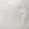 Nahaufnahme des weißen Schaums und der Blasen von Mario Badescu Acne Facial Cleanser, die auf dem Wasser schwimmen.