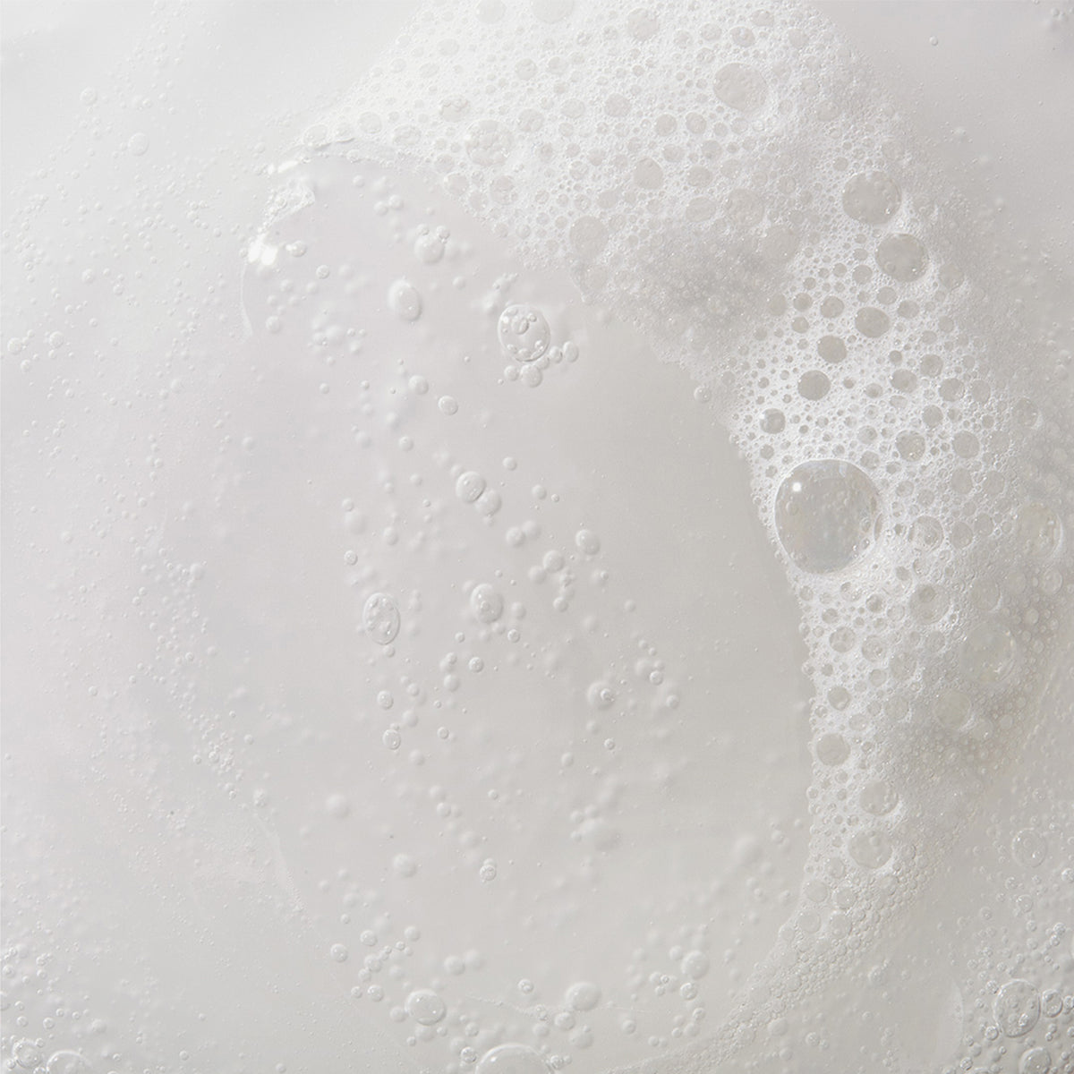 Nahaufnahme des weißen Schaums und der Blasen von Mario Badescu Acne Facial Cleanser, die auf dem Wasser schwimmen.