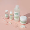 Vier Mario-Badescu-Produkte für unreine Haut auf rosa Hintergrund, mit Texturen und Wattestäbchen dekorativ arrangiert.
