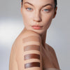Frau mit makellosem hellen Teint, auf deren Oberarm vier cremige Swatches des The Mood Contrast in verschiedenen Brauntönen aufgetragen sind.
